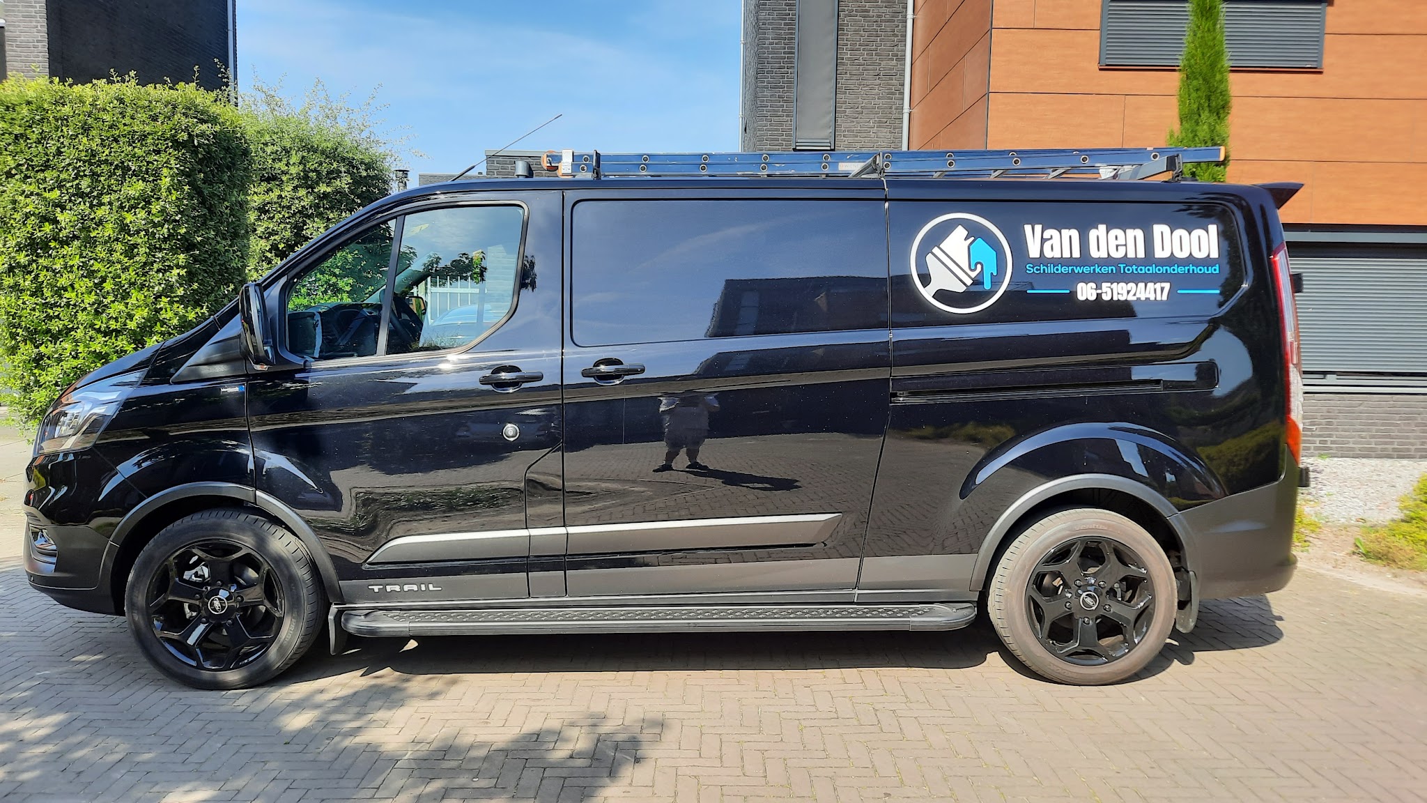 De zwarte bus van Van den Dool Schilderwerken Totaalonderhoud met logo en telefoonnummer