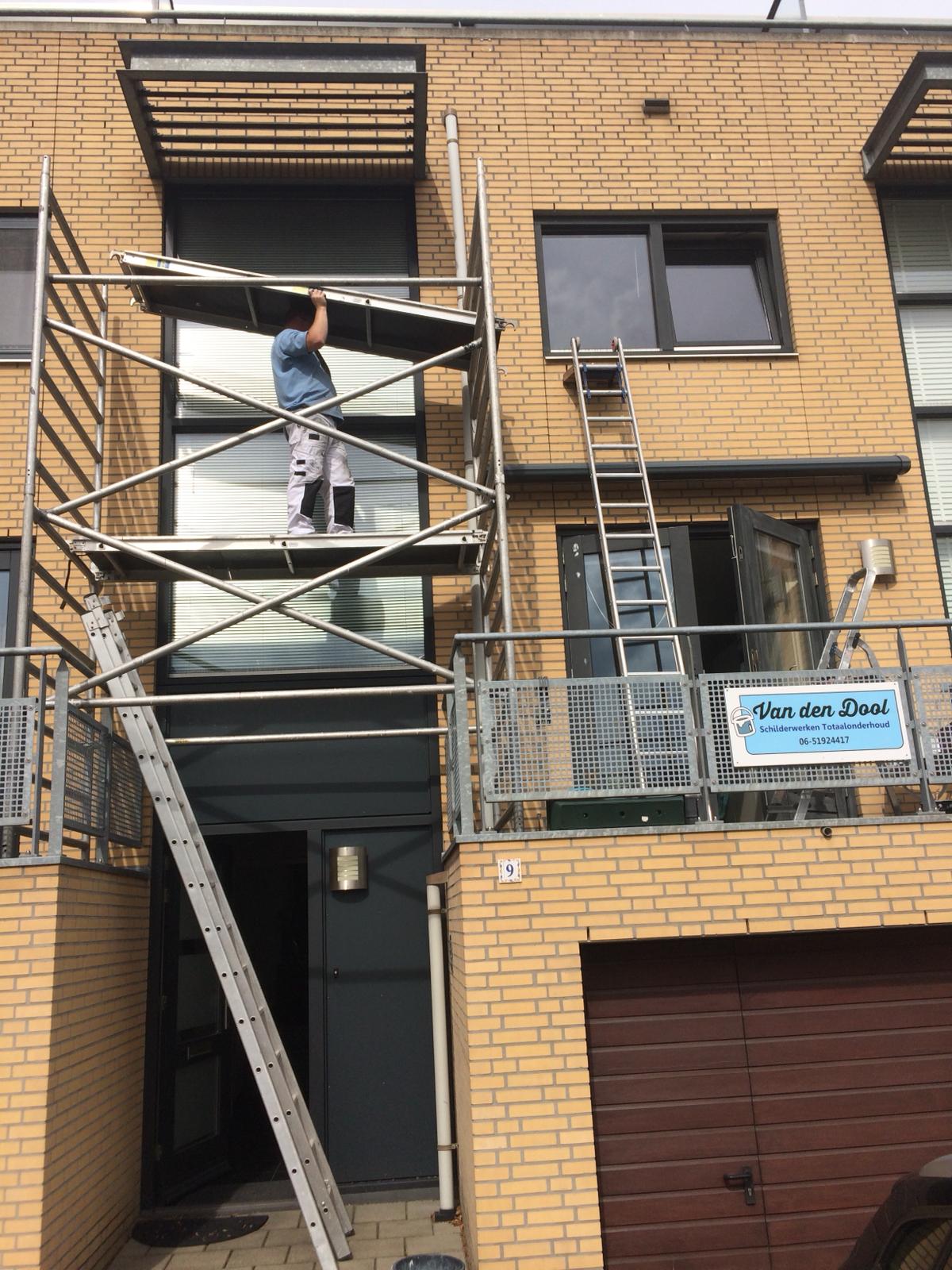 Schilder op de steiger bij een bakstenen gevel, met het bord van Van den Dool Schilderwerken